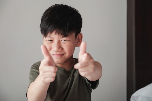 Smiling Asian tween boy pointing finger gun gesture, fun cheeky happy youth portrait