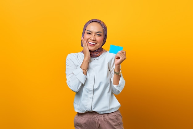 Smiling Asian woman holding blank card and touch her cheeks over yellow background