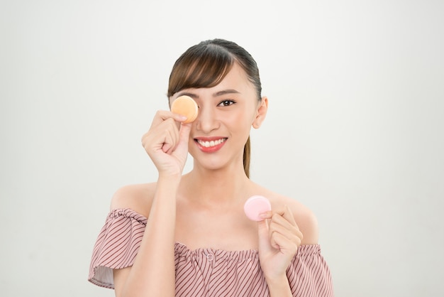 Smiling Asian woman holding Macaroons on her eyes.