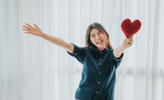 Smiling Asian woman showing red heart with open arms