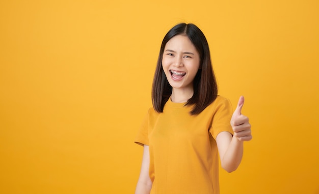 Smiling Asian woman and showing thumbs up or like on yellow background.