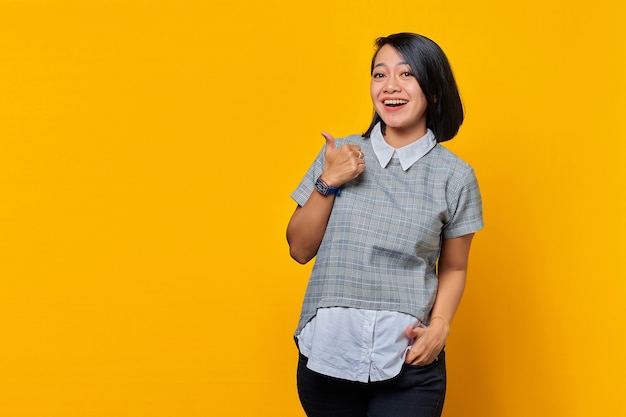 Smiling Asian woman showing thumbs up on yellow background