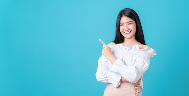 Smiling Asian woman stand and pointing finger on blue.