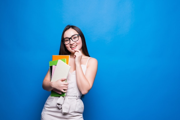 Smiling asian woman student holding books and file , college or school student and education concept isolated on blue wall with copy space.