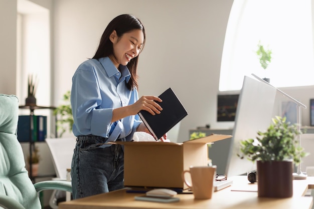 Smiling asian woman unpacking box at new workplace