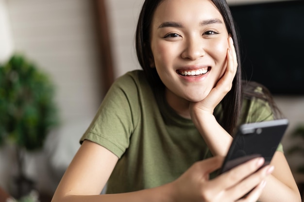 Smiling asian woman using mobile phone from home making order deliver smth to her house