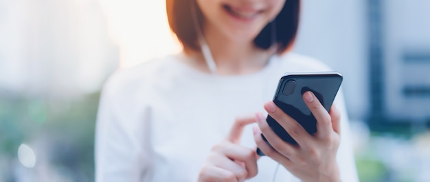 Smiling Asian woman using smartphone with listening to music and standing in office building