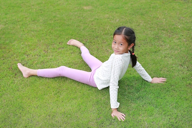 Smiling Asian young girl child lying on green lawn at the garden Kid lies on grass with looking camera