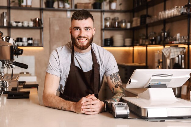 Smiling attractive man barista standing behind the counter at the coffee shop