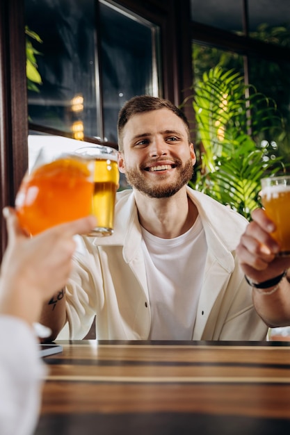 Smiling attractive man is drinking beer while sitting at in pub with friends company