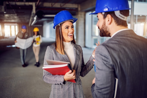 Smiling attractive positive female architect talking to her supervisor about ideas for interior design. Building in construction process interior.