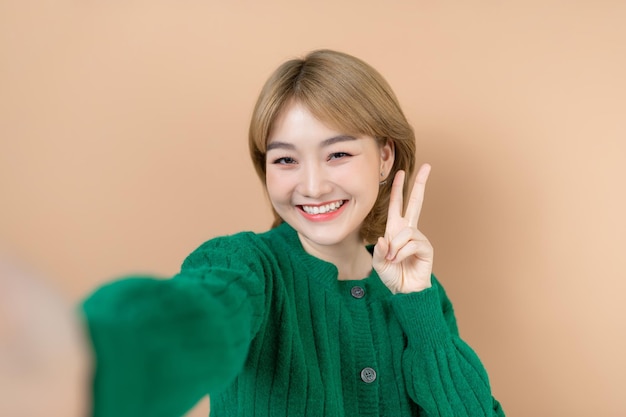 Smiling attractive young woman using mobile phone while standing isolated over beige background