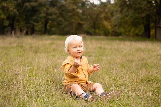 Smiling baby boy sitting in meadow in grass in autumn forest