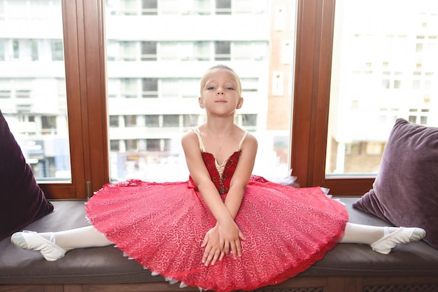 Smiling baby girl dreaming to become professional ballet dancer classical dance school the little girl ballerina does stretching sitting against the window