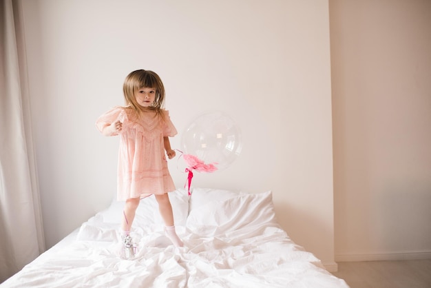 Smiling baby girl holding balloon jumping in bed close up