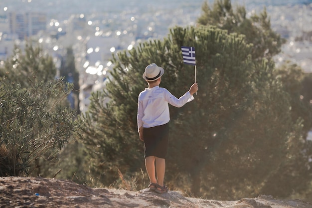 Smiling baby toddler boy holding a Greece flag on city background Independence Day Flag Day