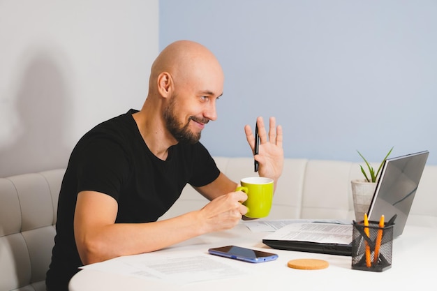 Smiling bald man with beard in black Tshirt working on his notebook at home side view