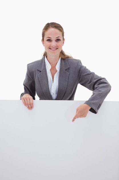 Smiling bank employee pointing down at blank sign against a white background