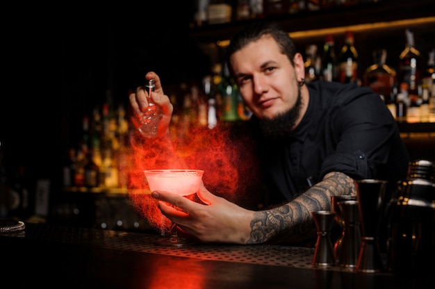 Smiling bartender spraying on the delicious cocktail from the special vaporizer on the bar counter