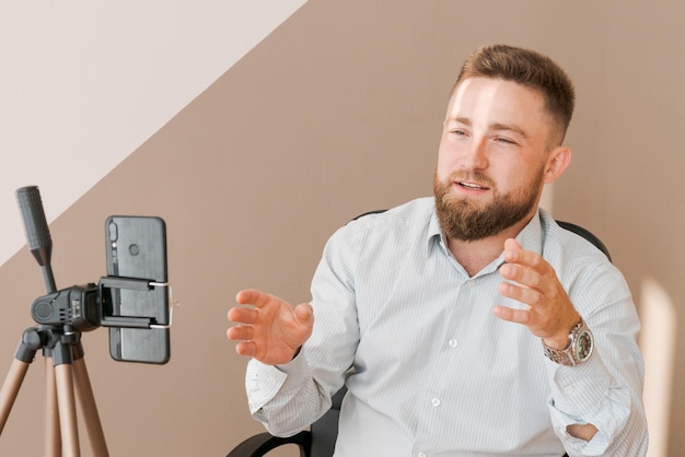 Smiling bearded business man filming his video blog episode using smartphone