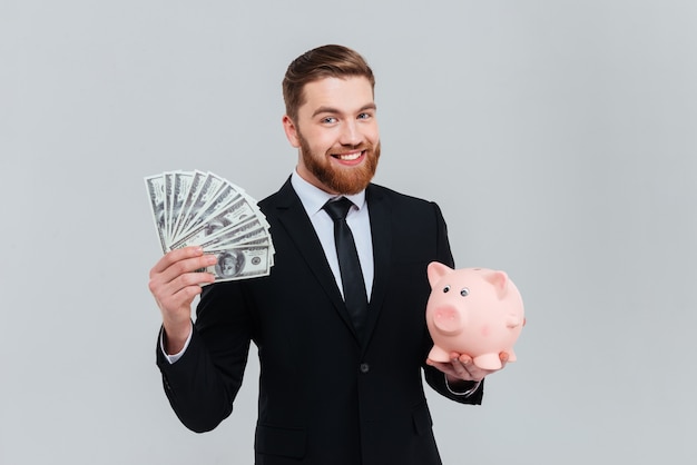 Smiling bearded business man in suit with money and money box