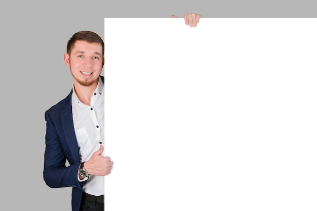 Photo a smiling bearded man shows a thumbs up gesture while holding onto a white blank board, standing on a gray background