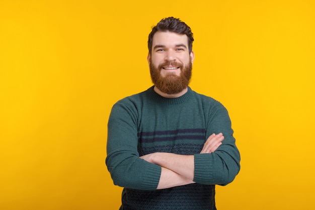 Smiling bearded man with arms crossed is looking at the camera over yellow space.