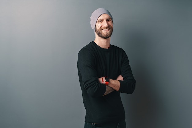 Smiling bearded young man with crossed arms on gray