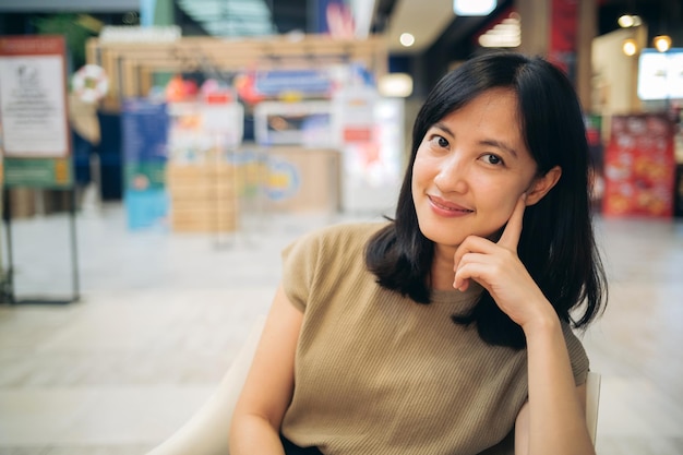 Smiling beautiful asian woman sitting in cafeteria at shopping mall