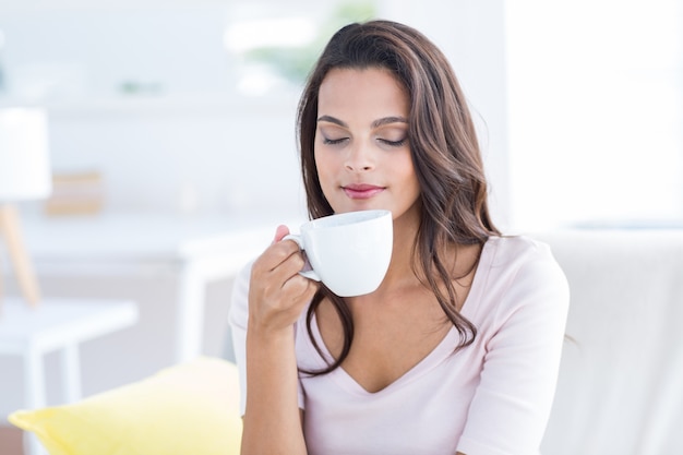 Smiling beautiful brunette relaxing on the couch and holding mug