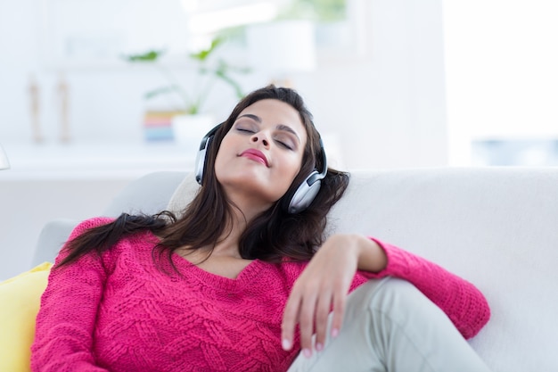 Smiling beautiful brunette relaxing on the couch and listening music