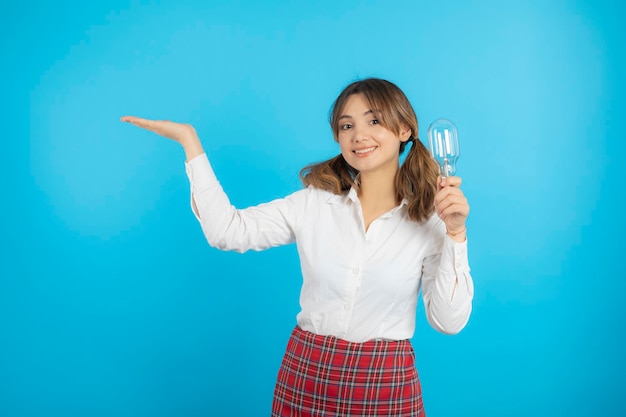 Smiling beautiful college girl holding idea bulb and raise her hand to the right side. High quality photo