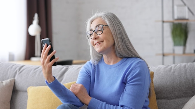 Smiling beautiful elderly gray-haired woman using smartphone