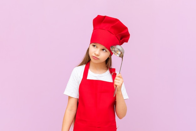 A smiling beautiful girl in a chef's costume on a purple background holds a ladle in her hands and smiles