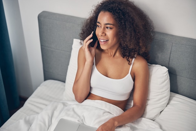 smiling beautiful lady in a top talking on her cellular phone in bed