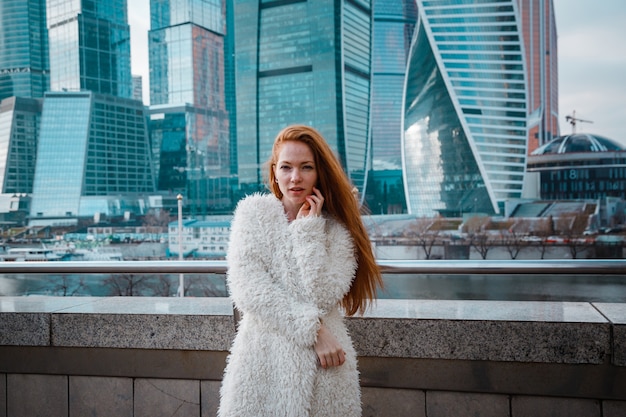 Smiling beautiful woman in a light coat against skyscrapers of a big city