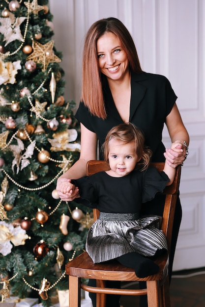 Smiling beautiful woman with her funny little girl near Christmas tree