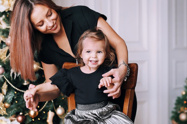 Smiling beautiful woman with her funny little girl near Christmas tree