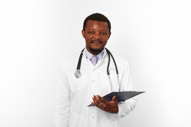 Smiling black bearded doctor man in white robe with stethoscope holds medical chart on clipboard