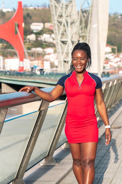 Smiling black girl of afro ethnicity walking down the city street in a colourful red sporty dress