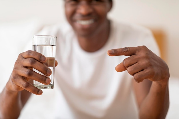 Smiling Black Guy Holding Glass Of Water And Pointing At It