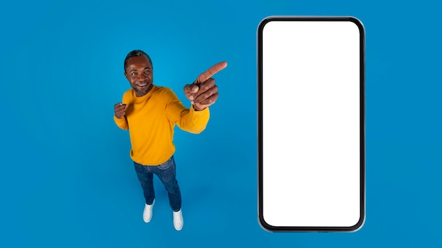 Smiling black man pointing at huge smartphone with blank screen