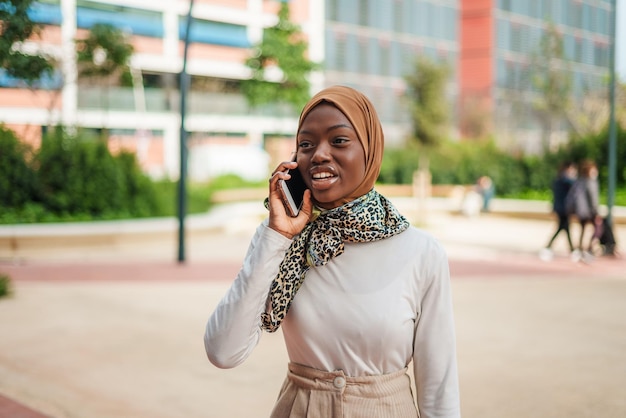 Smiling black woman in muslim headscarf talking on smartphone