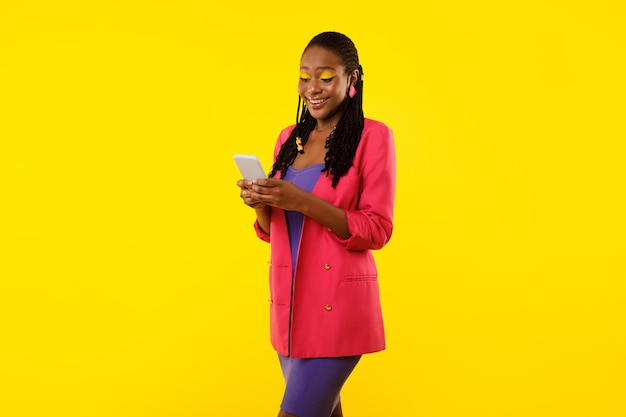 Smiling black woman using smartphone enjoying online communication yellow background