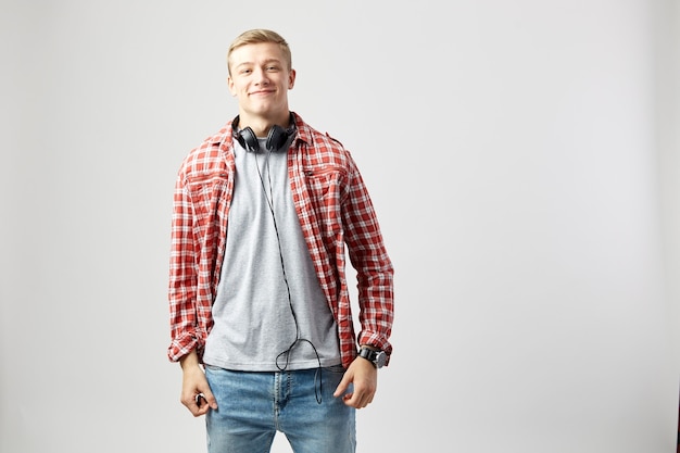 smiling blond guy with headphones on his neck stands on the white background 