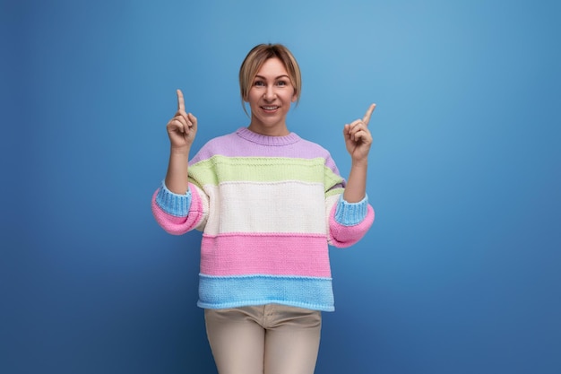 Smiling blond woman in a casual look demonstrates about the copy space on the wall on a blue