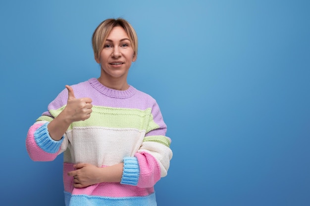 Smiling blond woman in casual outfit showing like on blue background with copy space