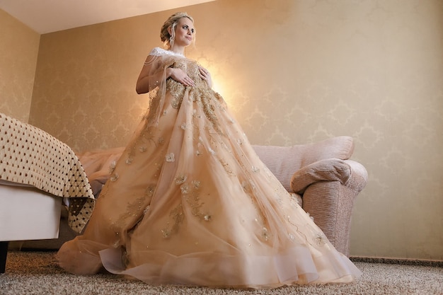 smiling blonde bride in a beige chic dress in a hotel room