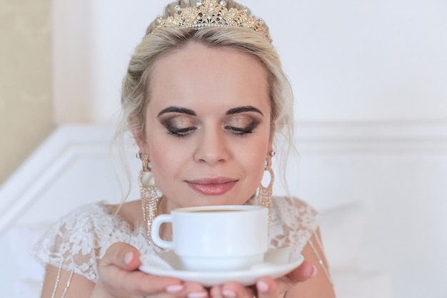 smiling blonde bride in a hotel room drinking coffee