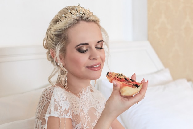 smiling blonde bride in a hotel room eating pizza